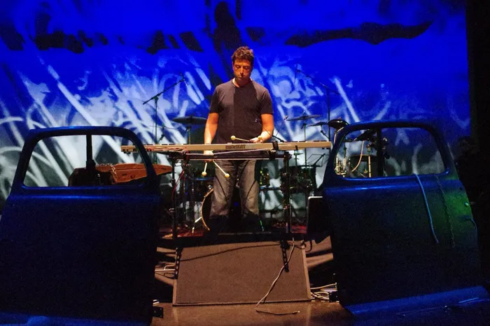 Steve Joslin playing drums with a red-lit backdrop
